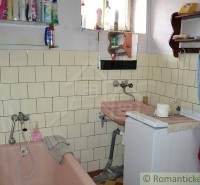 Bathroom of a family house with a bathtub, sink, washing machine, tiled walls, and shelves.