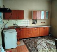 A kitchen in a family house with wooden cabinets, carpet, and a white countertop.