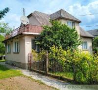 A family house in Košeca with a wooden fence and a garden, surrounded by greenery.