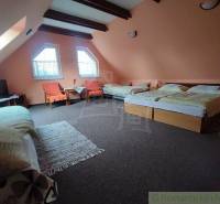 Attic room with five beds, TV, armchairs, and tables in a family house.