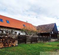 A family house with a wooden fence, a garden, and a pile of wood in the countryside.