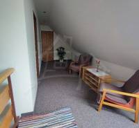 Attic space with chairs, a table, wooden elements, and a carpet in a family house.