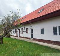 A country house with a red roof and a grassy garden, surrounded by trees.