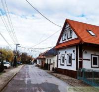 A rural street with a family house, red roof, sidewalk, blue fences, trees in autumn.