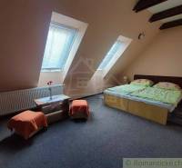 Attic bedroom with a double bed, skylights, orange chairs, and a table.