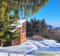 A snow-covered cottage in the middle of the forest with a view of the mountains and a family house.