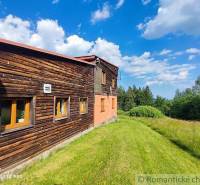A family house with a wooden facade surrounded by a green meadow and a blue sky.