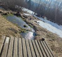 A wooden bridge over a stream, surrounded by a snowy mountain meadow and forest.