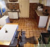 A kitchen in a family house with a tiled stove and a wooden table with a lace tablecloth.