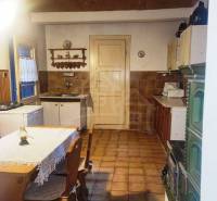 We see a traditional kitchen in an old family house with a tiled stove and wooden furniture.