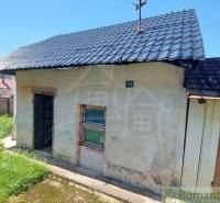 An older family house with a garden and a metal roof, surrounded by a wooden fence.