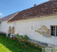 An old village family house with peeling plaster, sloping roof, green lawn.