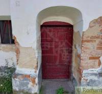 Old facade of a family house with peeling plaster, bricks, wooden door, window, greenery.