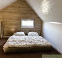 Attic bedroom in a cottage with a double bed and wooden wall paneling.