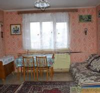 A room in an older family house with a sofa, table, chairs, and patterned wallpaper.