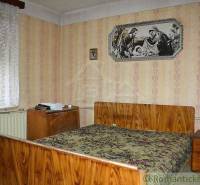 A bedroom in a family house with retro wallpaper, wooden furniture, and wall decorations.