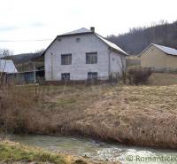 A family house by a stream in the countryside, surrounded by grassy areas in nature.