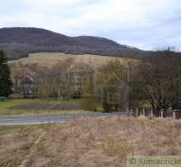 A rural view of agricultural and forest lands, surrounded by mountains and a road.