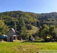A family house in a quiet nature, surrounded by trees, with hilly landscape in the background.