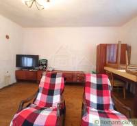 A room in a family house with armchairs, a television, and old furniture on a wooden floor.