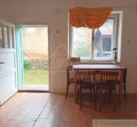 Rustic interior of a family house with wooden furniture, view of the yard, and open doors.