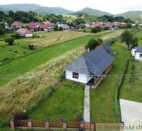 A wooden cottage surrounded by picturesque countryside and mountains on the horizon.
