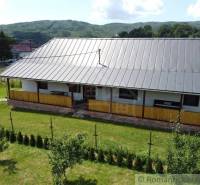 A cottage in picturesque nature with wooden verandas and a roof, surrounded by a garden with coniferous trees.