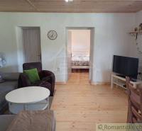 Living room of the cottage with wooden flooring, a sofa, a television, and a dining table.