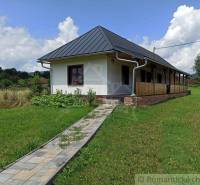 In the picture, there is a country cottage with a porch and a paved path in a natural setting.