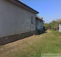 A family house with white plaster, a stone foundation, surrounding garden, and blue sky.