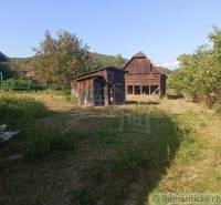 Garden area with a wooden cottage and a family house in a picturesque natural setting.