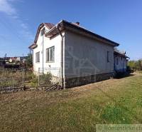 In the picture, there is an older family house with a lawn and a fence, surrounded by a garden.