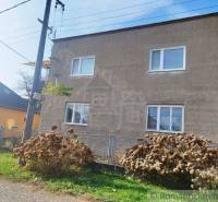 A family house with a gray facade, windows, an electric pole, and a fence.