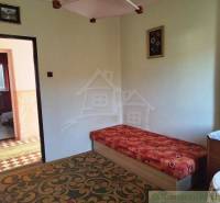 A room with older furniture, carpet, wallpaper, a painting, and a view into another room.