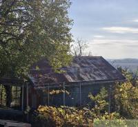 An old cottage in a natural setting with deciduous trees and a view of the surrounding landscape.