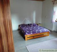 A bedroom in a family house with a wooden bed, purple bedding, and a small rug.