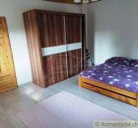 A bedroom in a family house with wooden furniture, a bed, and a wardrobe on a light floor.