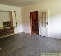 In the picture, there is a simple room with a cross, a radiator, and a painting in a cottage.
