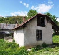 In the picture, there is an old cottage surrounded by nature and greenery, a blue sky, a chimney.