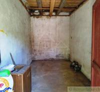 An older garage room with a wooden ceiling and simple walls in a cottage.