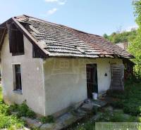 An old cottage with a damaged roof, surrounded by greenery, in a rural setting.