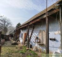 An old cottage with worn plaster and a wooden roof, surrounded by nature.