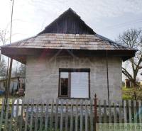 A traditional country cottage with a shingle roof and a fence in the garden.