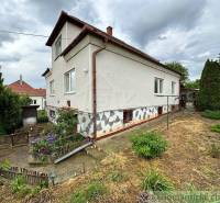 A family house with a white facade, garden, trimmed plants, fence, cloudy sky.