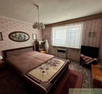 A bedroom in a family house with a floral blanket, vintage wallpaper, and classic furniture.