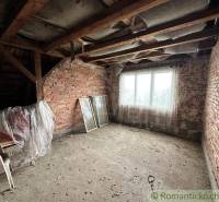 The attic of a family house with an exposed brick wall, old furniture, and a window frame.