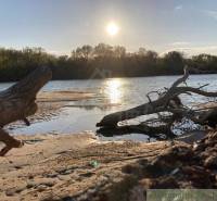 A river scene with a sandy shore, the reflection of the sun creates a serene image of the landscape.