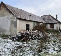 An old family house in the countryside, a snowy yard, a pile of wood, a typical village.