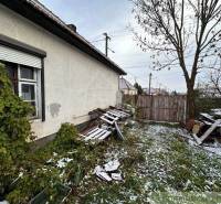 A family house with an unkempt yard, wood, and a gate covered in snow in winter.