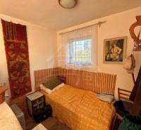Small room, bed with an orange throw, window, painting, cabin decoration.